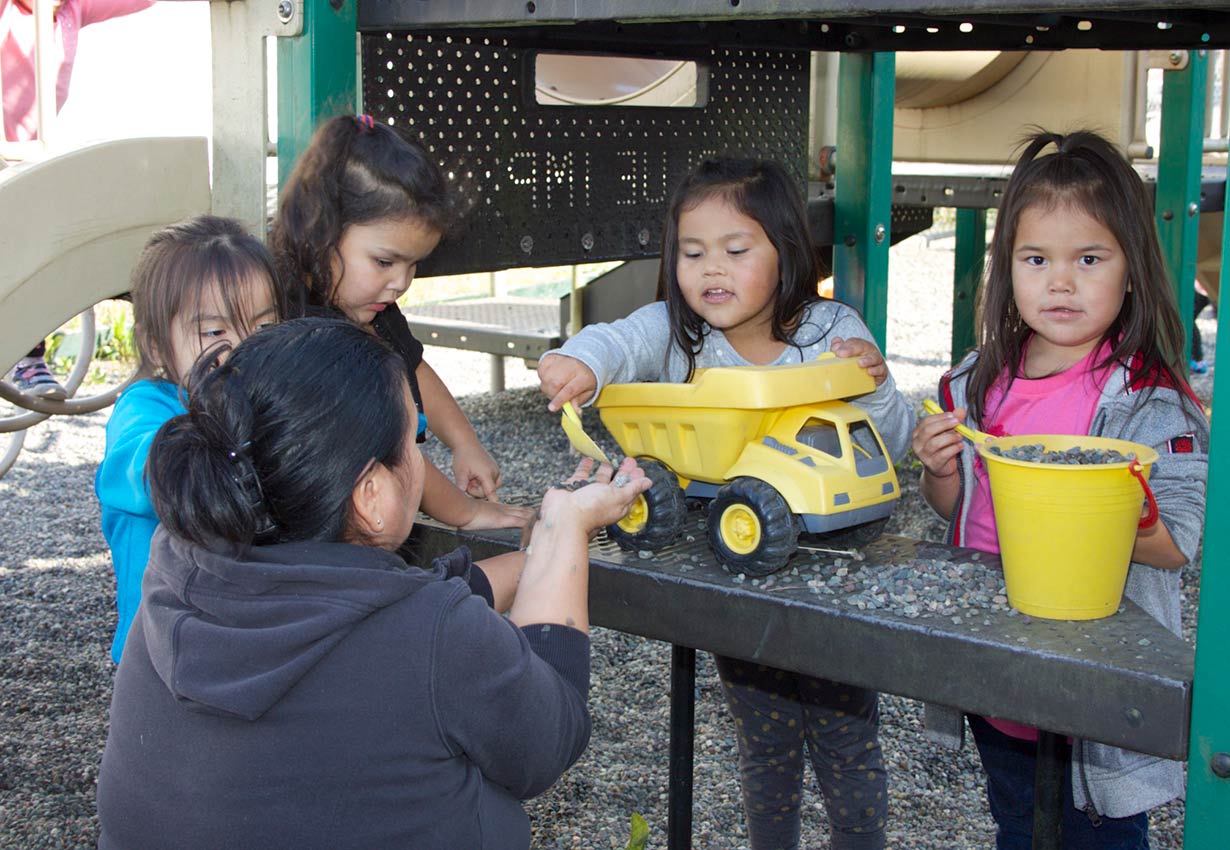 young children playing outdoors with trucks with an early childhood educator